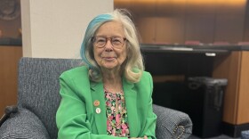 Woman in glasses and bright green blazer sitting smiles at camera