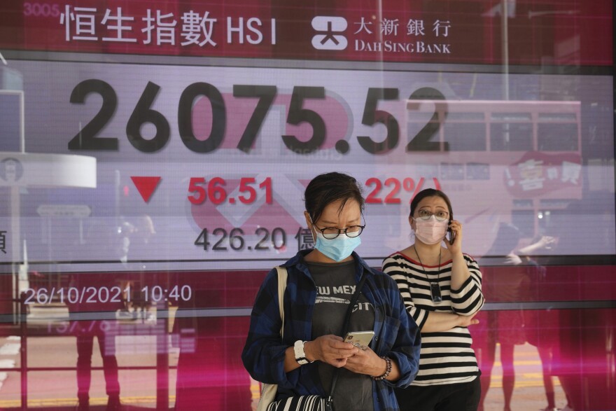 People wearing face masks walk past a bank's electronic board showing the Hong Kong share index in Hong Kong, Tuesday, Oct. 26, 2021. (AP Photo/Kin Cheung)