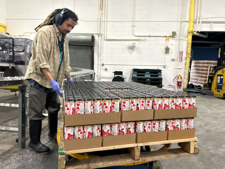 A Nine Pins Ciderworks employee with cases of the company's product. For its cans, the North Albany business needs aluminum sheets imported from Canada. That aluminum is now subject to steep tariffs, raising the company's canning costs.