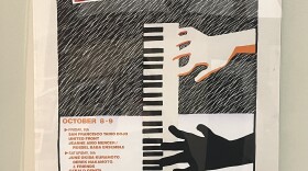 Close up of a poster on display. The poster reads "ASIAN AMERICAN JAZZ FESTIVAL" with a large cartoon graphic of two hands playing piano. 