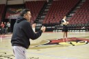 Man blowing a whistle and clapping while leading practice in a college basketball arena