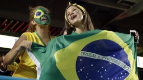 Two girls with green and yellow face paint hold a Brazilian flag