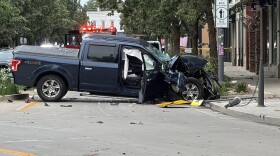 A damaged pickup truck sits on a city street in a small downtown area