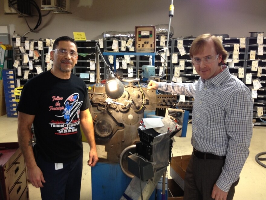 Juan Delgado (left) and Steve Kempf of Brooklyn's Lee Spring company stand with a 50-year-old coiling machine, still in use today.