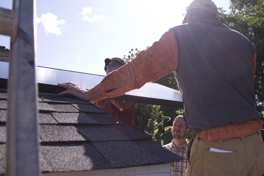 Volunteers pass a solar panel onto one of the installation roofs at Gemeinschaft.