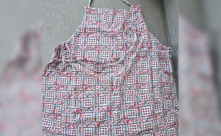 An apron with a strawberry and teapot pattern against a gray background.