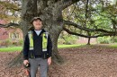 A man in a safety vest stands in front of a large tree