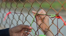 Two child hands pass red and green string through a fence