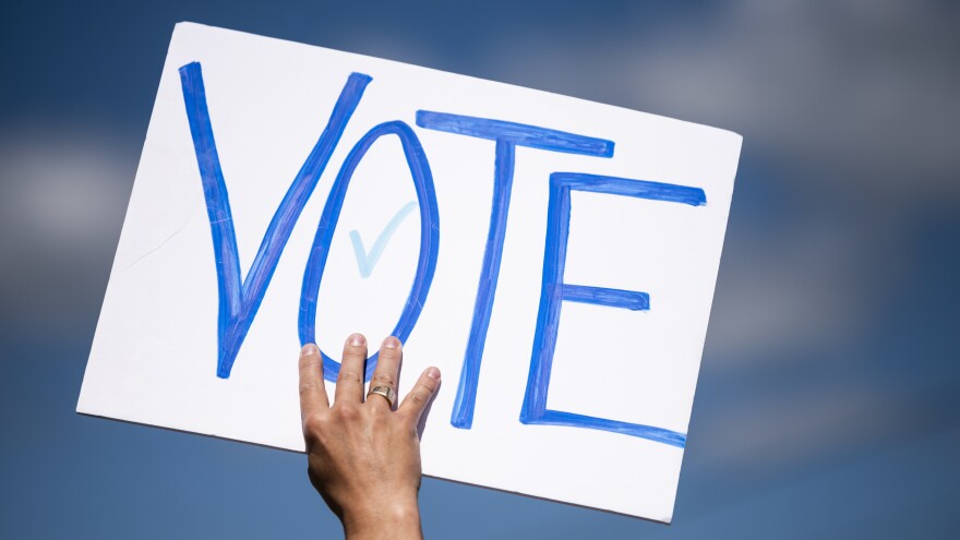 A man holds a sign that says "VOTE" outside Mankato Regional Airport as President Trump makes a campaign stop on Aug. 17 in Mankato, Minn. Both Trump and Democratic nominee Joe Biden visit the state Friday.