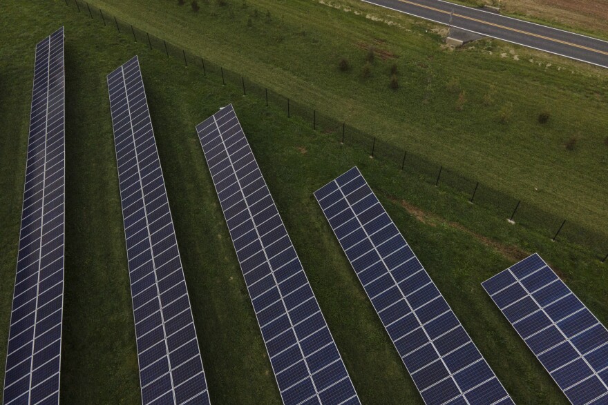 An overhead view, perhaps from a drone, of five rows of solar panels in a green field.