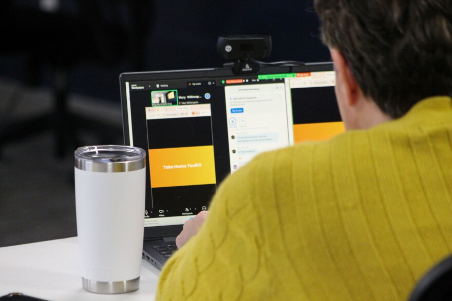 An Arc of DFW Area volunteer shares the presentation in a Zoom room. The volunteer wears a mustard yellow knit cardigan and has a white coffee thermos next to the computer streaming the training. On the computer is a slide that reads "Take home toolkit" and the Zoom chat box is open with many messages.