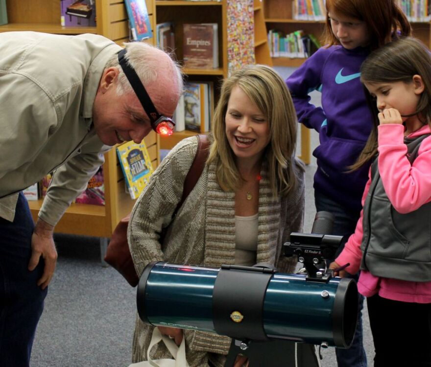 Elizabeth Gremaud (in purple) watches with her mom, Julie, and younger sister, Gabrielle, as the St. Louis Astronomical Society's Don Ficken demonstrates how to use a red-light headlamp to read the telescope's instructions in the dark.