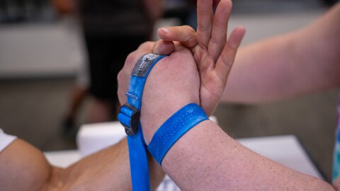 Two hands grip each other in an arm wrestling lock with a blue strap tying them together.