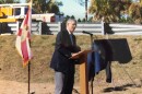 A gentleman wears a suit at a podium at construction of a road to talk to those present