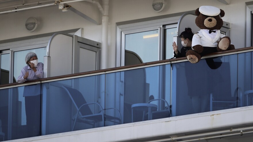 A woman with a teddy bear waves to another passenger as they undergo quarantine on the Diamond Princess cruise ship in Yokohama, Japan. Many passengers are using chat groups and social media to share information with each other.