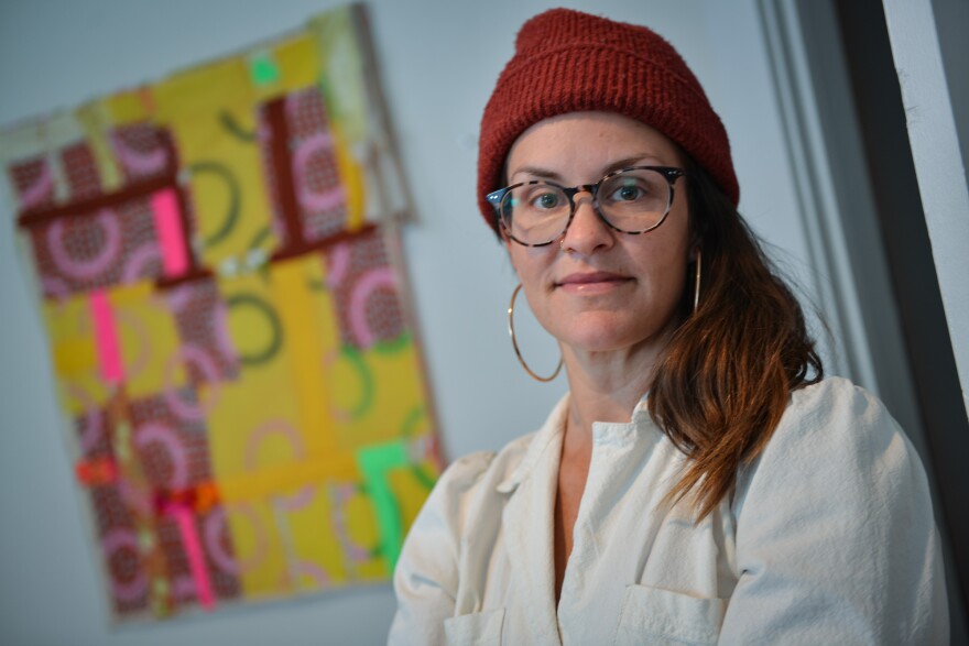 Textile artist Jessica Rogers stands in her home studio next to a piece of fabric that inspired her contribution to a dress in the Coalesce fashion show.