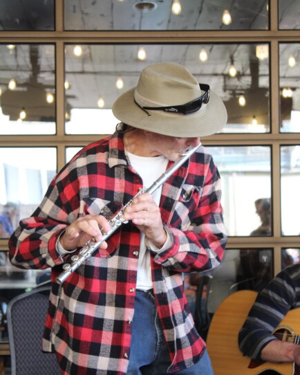 A flute player in a hat stands while playing music with others.