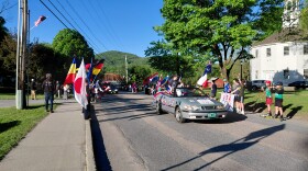 Children with flags flank a silver convertible during a parade.
