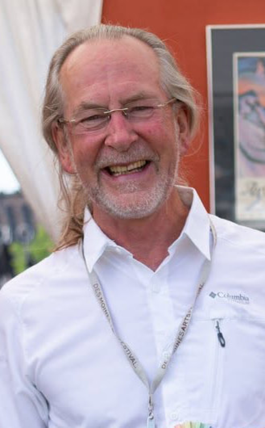 A man standing and smiling wearing a white shirt and glasses