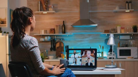 Woman falling asleep during video conference on laptop working from home late at night in the kitchen.