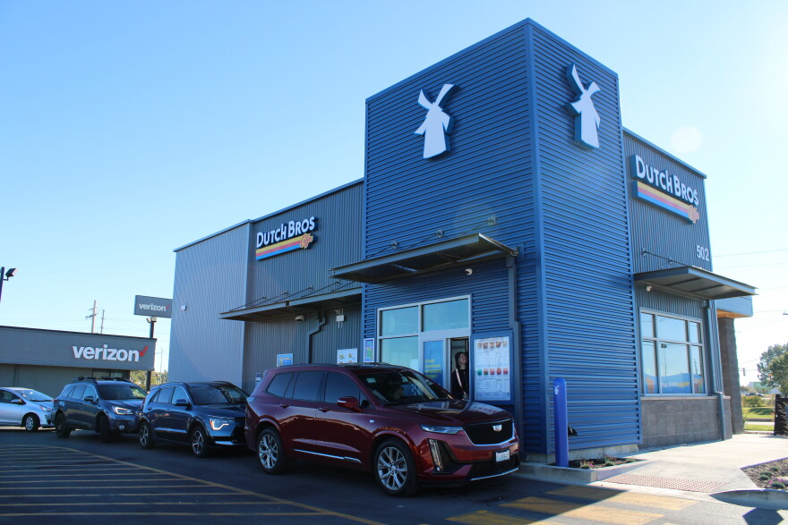 A line of vehicles wait for coffee from a large blue building that says "Dutch Bros"
