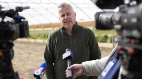 U.S. Rep. Eric Sorensen talks to media on a farm while wearing a forest green quarter-zip sweater