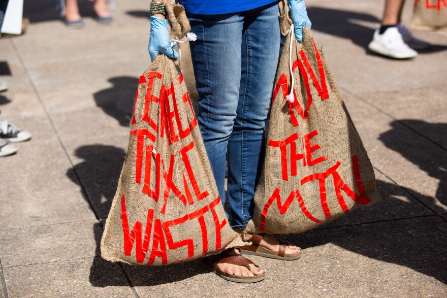 An activist carries two bags of shingles, with the phrases, “Clean Toxic Waste” and “Move The Mountain,” during today’s Shingle Mountain relocation action at Dallas City Hall.