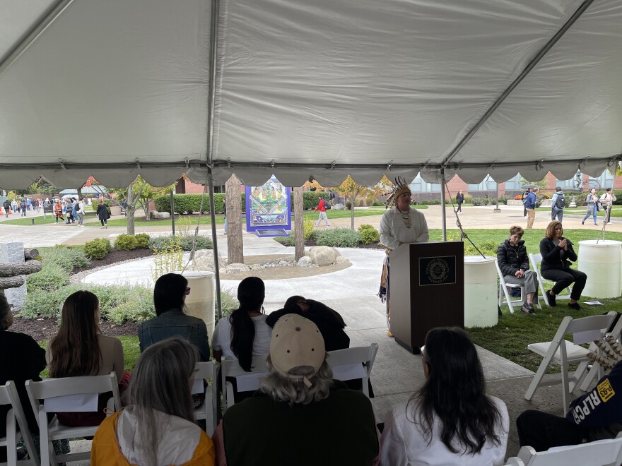 A crowd sits under a tent as Brandon Lazore stands behind a podium speaking.