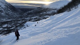 Skiers head down a snowy valley.
