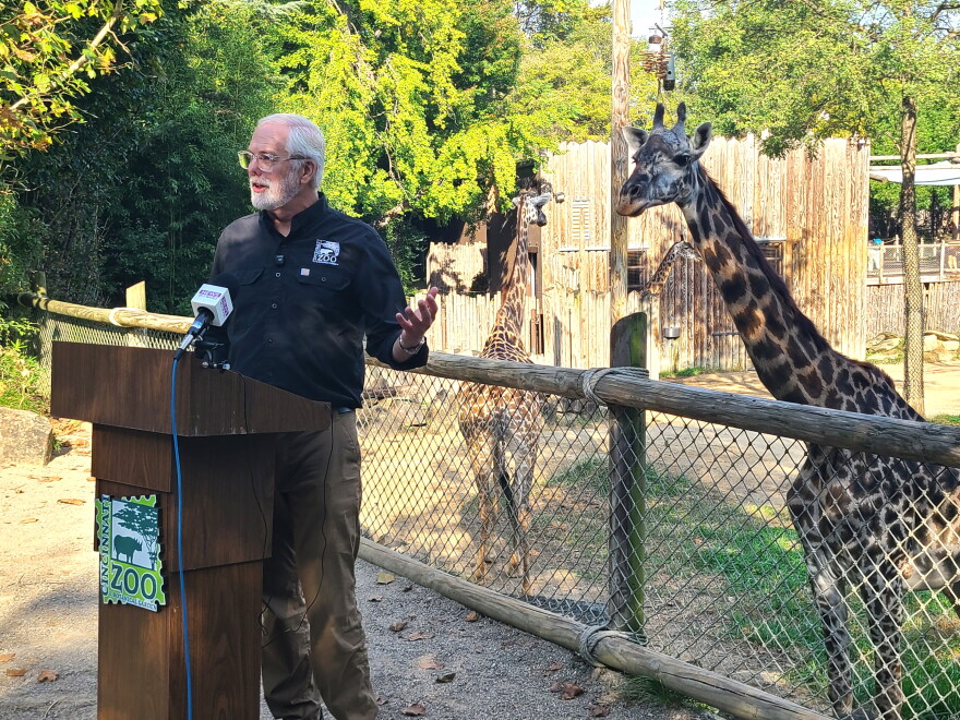 man at a podium with a giraffe behind him