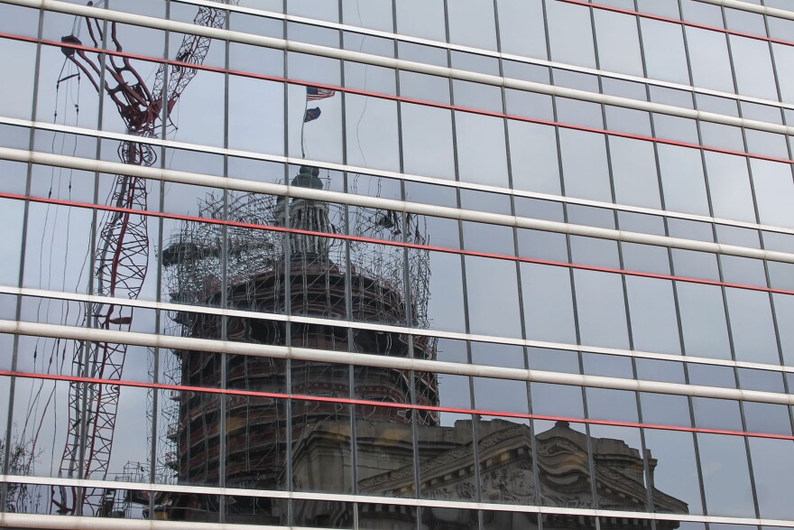 The Indiana Statehouse dome is reflected in a bank of windows of a building across the street.