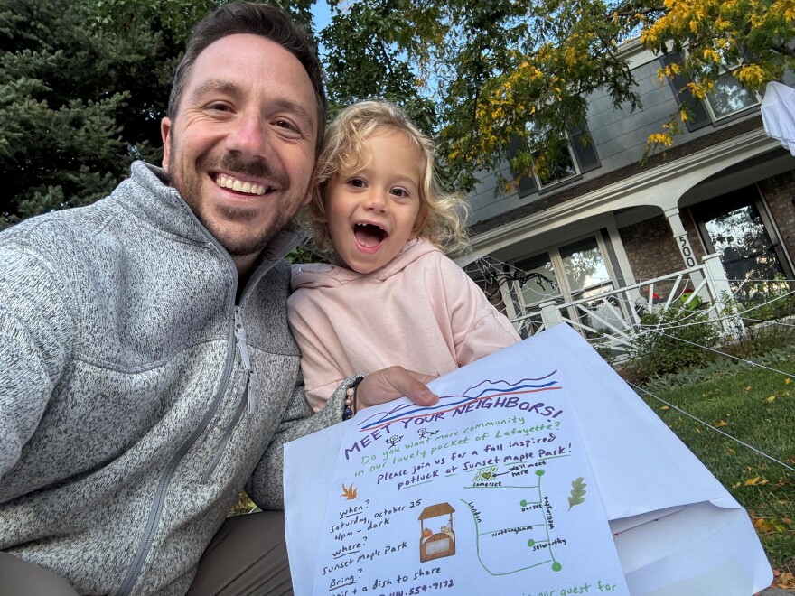 A dad and his young daughter smile for a selfie in front of a house. They're holding a handmade flyer inviting people to a community event. The main text reads "Meet Your Neighbors!!"