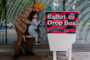FILE - Matt lifts up his three-year-old son, Theo, to cast his ballot into the Hillsboro Public Library-Shute Park ballot drop box in May 2026. Election officials are increasingly recommending voters plan to use drop boxes rather than mailing their ballot.