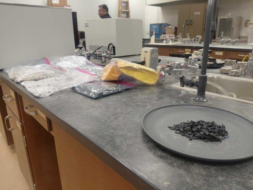 A plate with black asphalt particles sits on a table in a lab.