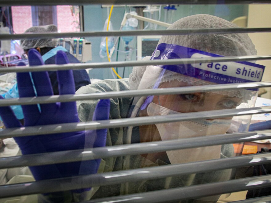 Respiratory therapist Miriah Blevins — in full personal protective equipment — peers out a window looking for assistance as she cares for a patient.