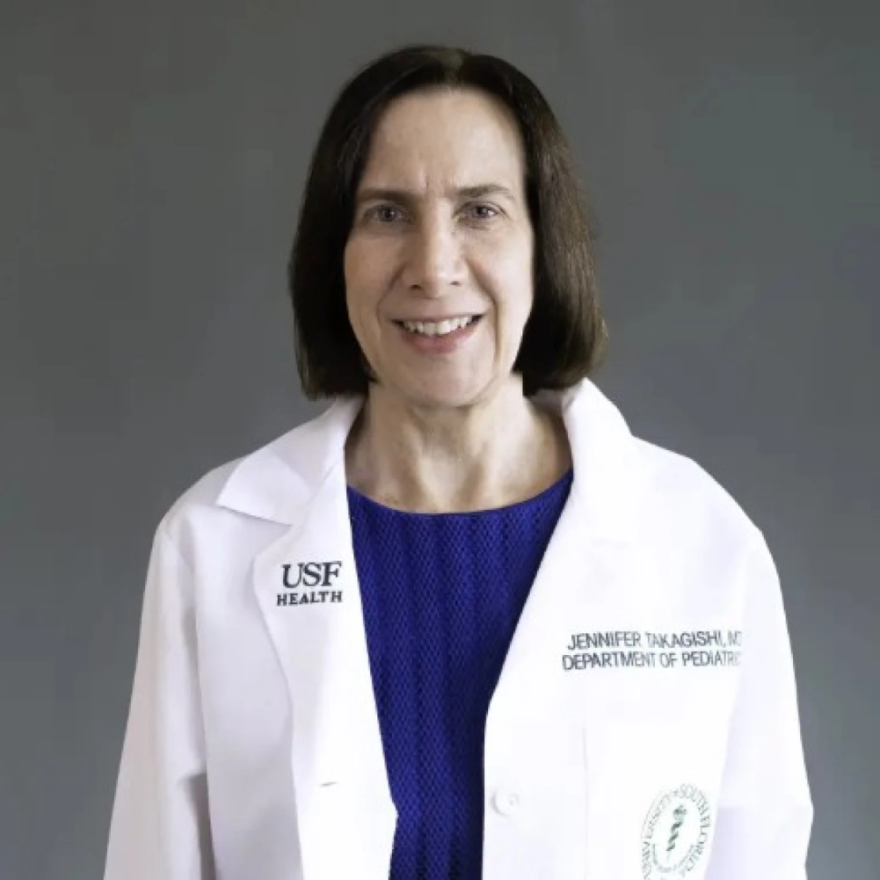 Mujer de cabello castaño corto, con una bata blanca de laboratorio y una blusa azul oscuro, sonriendo a la cámara.