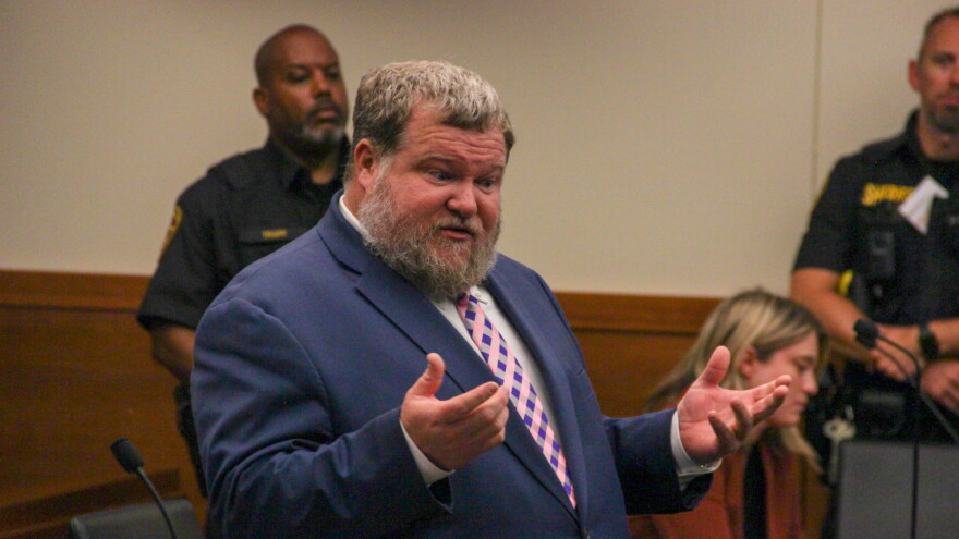 A man in a suit speaks in a courtroom. 
