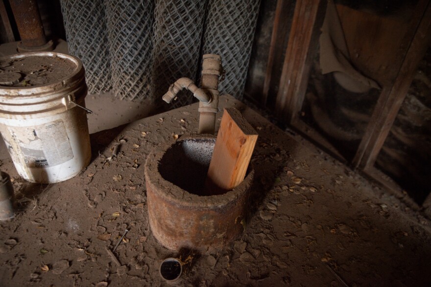 photo shows a dusty, decommissioned well with a plank of wood sticking up out of the center.