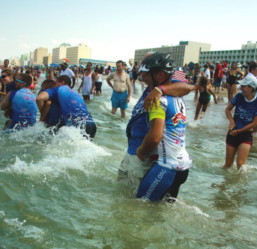 People wearing bicycle gear celebrating a long ride across country wade into the Atlantic Ocean.