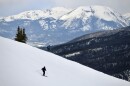 A pair of skiers descends a snowy slope with a view of snow-covered mountains in the distance.