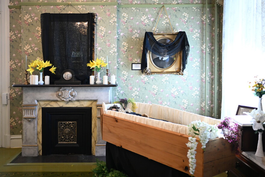 A wooden coffin sits below a portrait draped in black