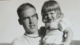 Black and white photo of smiling young girl in a white dress, held by young man looking pensive