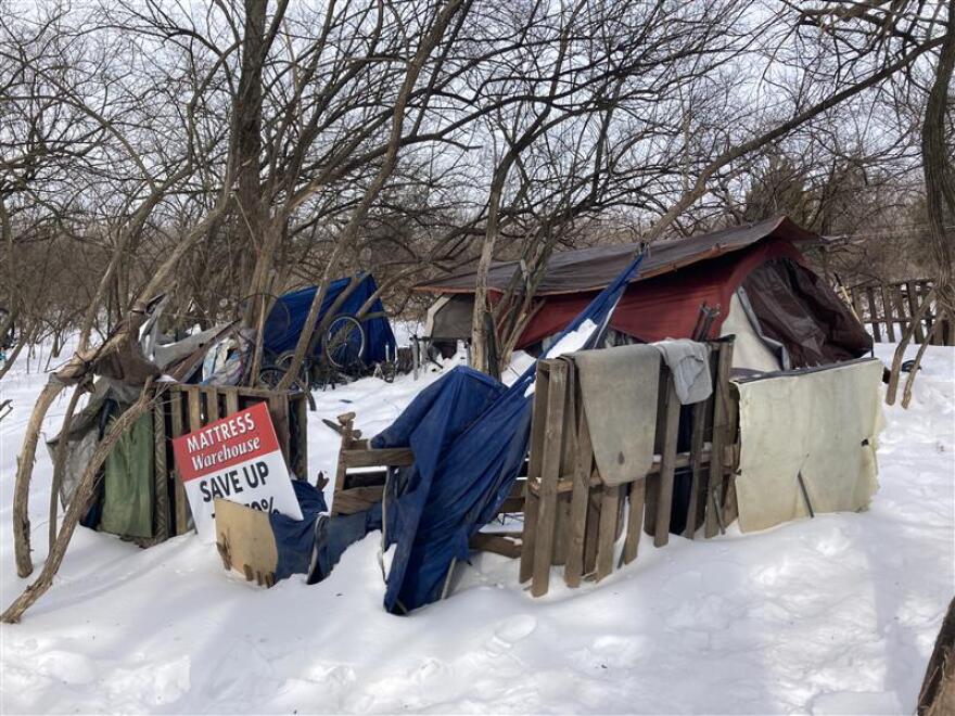 A shelter made of a tent and tarps with a wooden pallet fence.