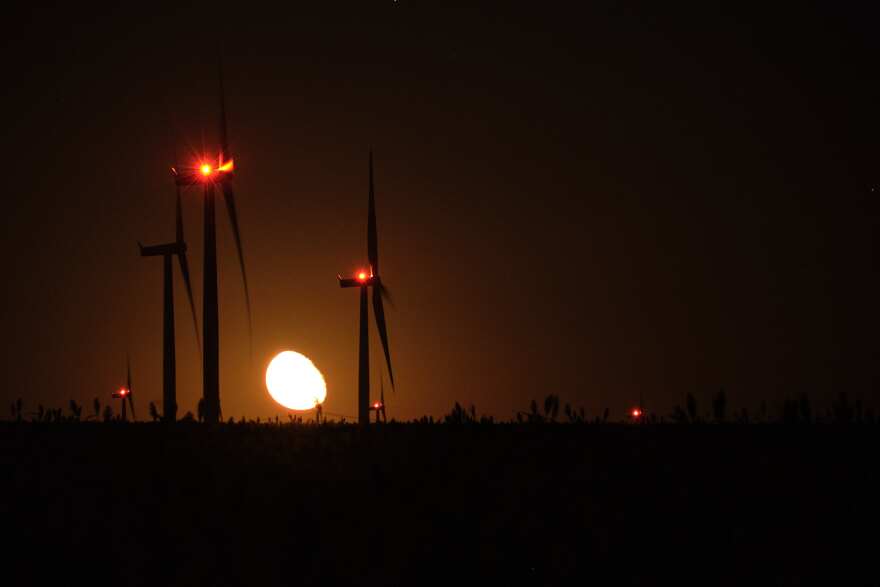 A photo shows wind turbines silhouetted against the sunset.