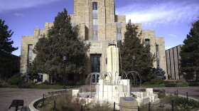 A strange white stone fountain with metal streamers instead of water sits outside a regal faded white stone building with the word courthouse etched above the front door