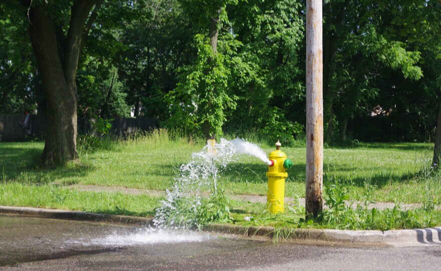 A yellow fire hydrant, turned on by city workers, is pouring out water to help residents in Kalamazoo cool off during extreme heat.