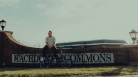 Brett Zupka sits on a brick wall with the Macedonia Commons sign on it