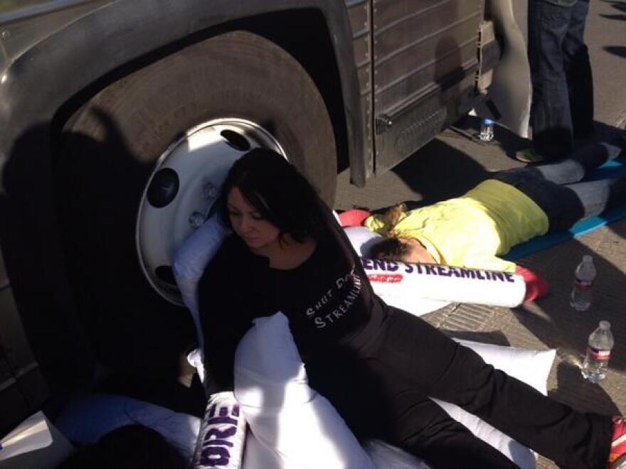 A protester chained to the wheel of a bus carrying people to deportation hearings in Tucson