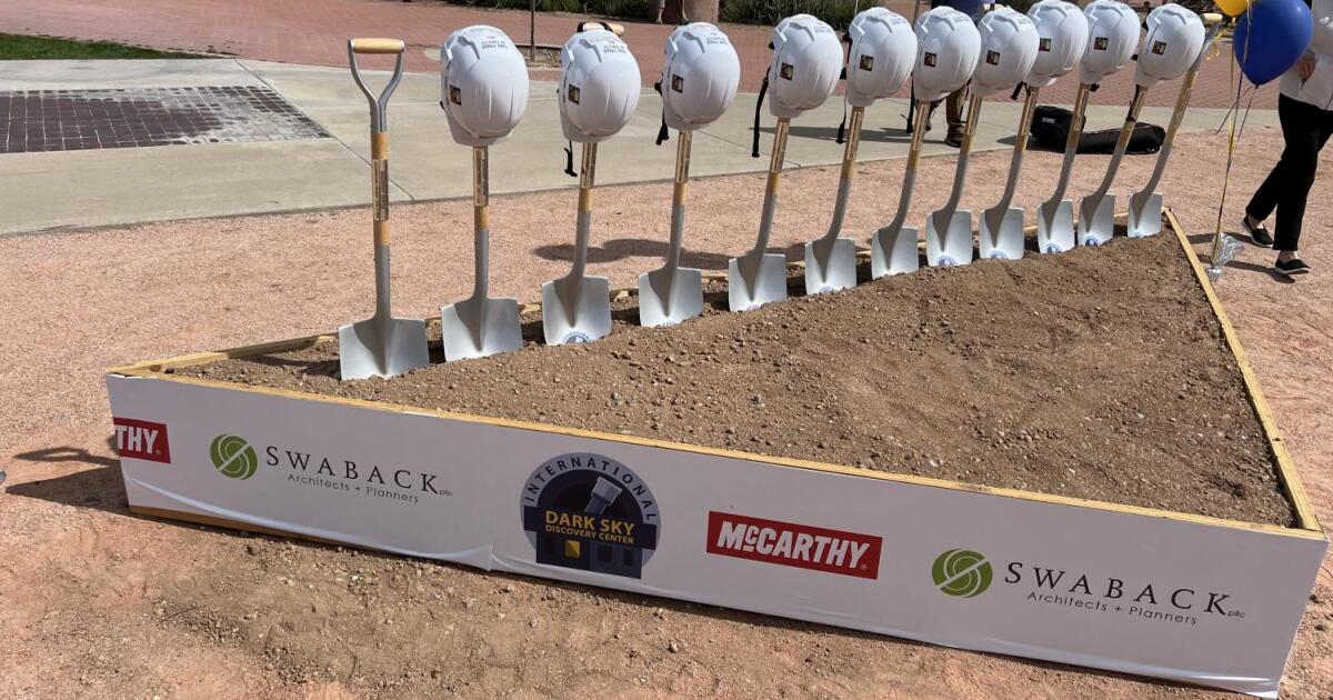A dozen ceremonial shovels topped with hardhats are placed into a triangular bed of dirt
