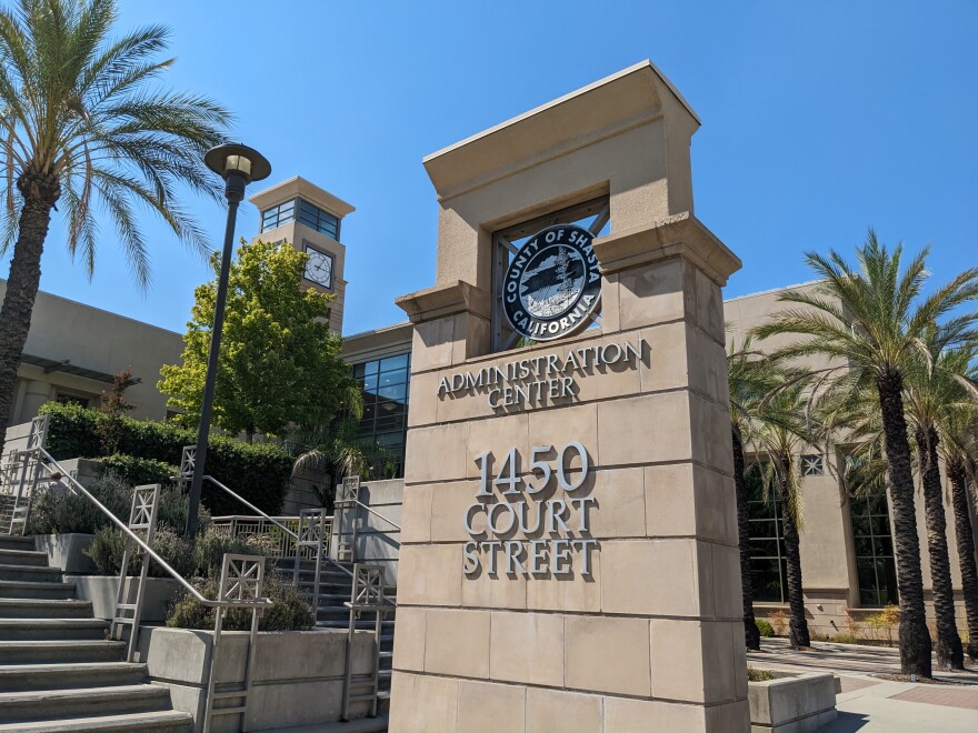 A sign in front of a large building with a clock tower on top. The sign says "County of Shasta California, Administration Center, 1450 Court Street."